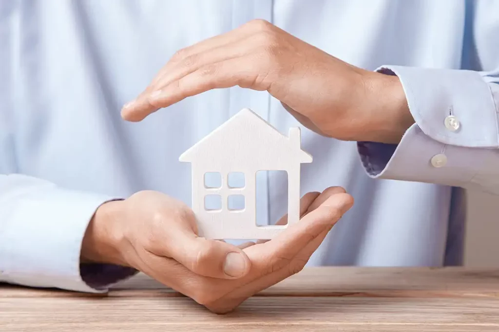 Hands gently covering a miniature white house model, symbolizing homeowners insurance and protection for new construction homes.