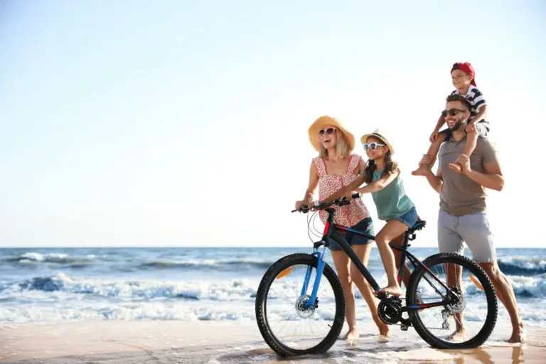 Family having fun at the beach in Vero Beach, Florida, with a mother and daughter riding a bike along the shore and the father carrying his son on his shoulders.